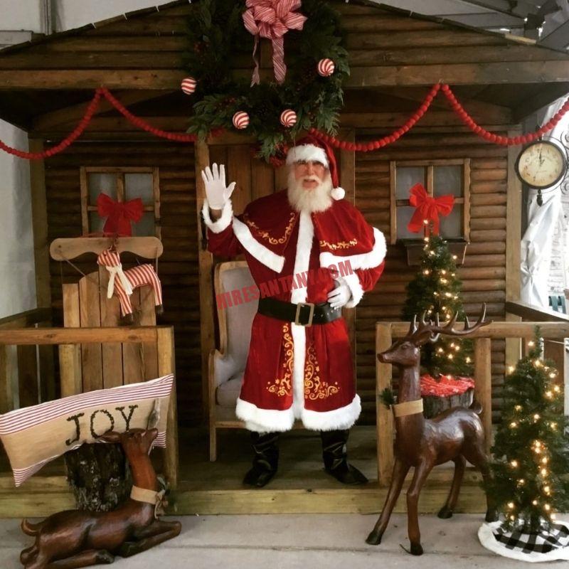 Real bearded Santa for hire in New York City waving from a cabin set with wooden reindeer
