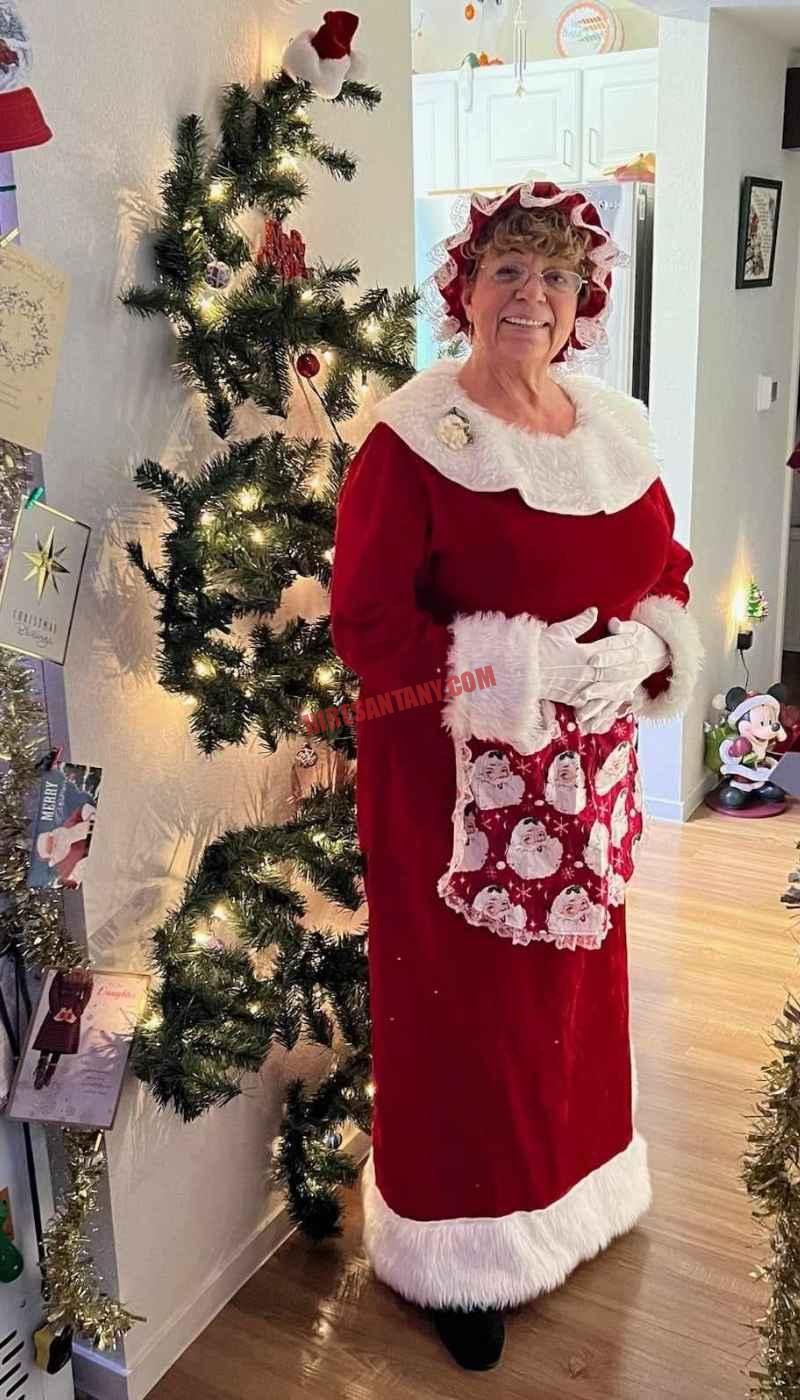 Mrs. Claus for hire in NYC standing beside a slim lit Christmas tree in a hallway